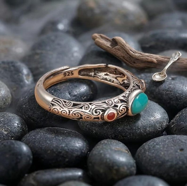 Peut inclure: Une bague argent&eacute;e &agrave; anneau ouvert orn&eacute;e de gravures complexes en volutes, d'une petite pierre ronde rouge et d'une pierre ovale plus grande de couleur turquoise. L'int&eacute;rieur de l'anneau porte l'inscription 925, indiquant de l'argent sterling.