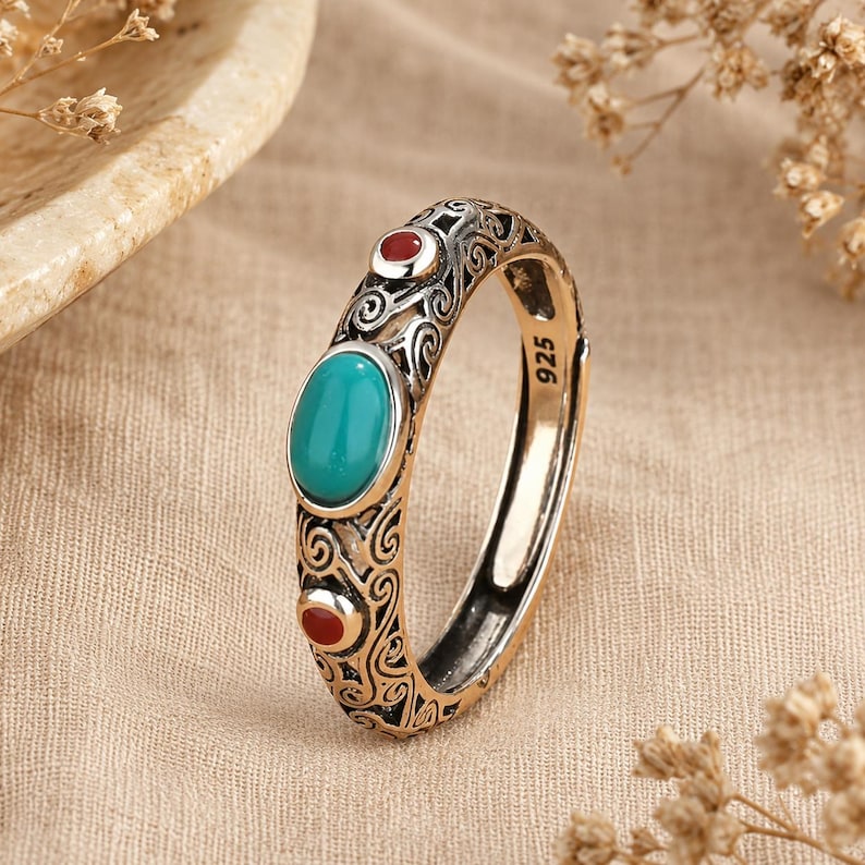 Peut inclure: Une bague en argent sterling avec un poin&ccedil;on 925, orn&eacute;e d'une pierre centrale ovale de couleur turquoise et de deux petites pierres rondes rouges. L'anneau est d&eacute;cor&eacute; de motifs de volutes complexes sur toute la surface m&eacute;tallique.