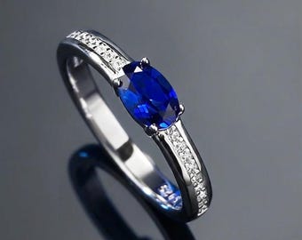 Peut inclure: Une bague argentée ornée d'une pierre précieuse bleu foncé taille ovale fixée par quatre griffes. L'anneau est agrémenté d'un canal de petites pierres claires serties pavé le long de la tige, avec l'inscription 925 gravée à l'intérieur.