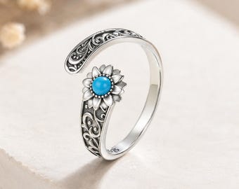 Peut inclure: Une bague ouverte en argent avec une finition oxydée et des motifs de volutes complexes. Une extrémité de l'anneau présente un motif de tournesol détaillé avec une petite pierre turquoise ronde et brillante au centre. L'anneau porte le poinçon 925.