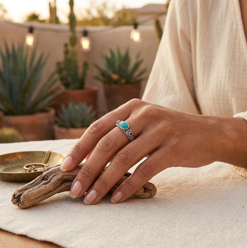 Peut inclure: Une bague en argent orn&eacute;e d'une pierre turquoise ovale centrale, entour&eacute;e de deux petites pierres rouges rondes. L'anneau pr&eacute;sente un travail de m&eacute;tal textur&eacute; et complexe avec des d&eacute;tails oxyd&eacute;s, offrant un aspect vintage au doigt.
