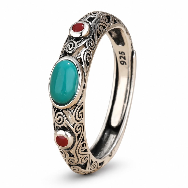 Peut inclure: Une bague en argent sterling orn&eacute;e d'une pierre ovale de couleur turquoise au centre, flanqu&eacute;e de deux petites pierres rondes rouges. L'anneau pr&eacute;sente des motifs de volutes complexes et porte l'inscription 925 grav&eacute;e &agrave; l'int&eacute;rieur.