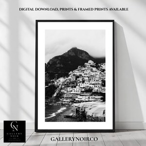 May include: A black and white framed wall art print depicting a coastal hillside town with stacked buildings, a mountain peak, and beach umbrellas. The text reads: DIGITAL DOWNLOAD, PRINTS & FRAMED PRINTS AVAILABLE and GALLERY NOIR CO.