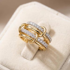 Puede incluir: Un anillo de varias bandas con bucles de oro entrelazados y bandas de diamantes en pavé. El diseño consiste en eslabones de oro amarillo pulido que se alternan con bandas incrustadas de pequeñas piedras claras y brillantes, creando un aspecto texturizado.
