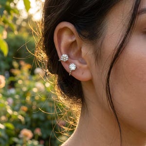 Puede incluir: Dos pendientes tipo ear cuff de tono plateado, cada uno con una piedra redonda, transparente y facetada en un engaste de garras. Los pendientes se sitúan a lo largo del borde exterior del cartílago de la oreja, con un acabado brillante.
