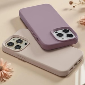 May include: Two silicone smartphone cases, one in a muted lavender purple and the other in a soft beige, each featuring a square camera cutout with three circular lens openings and raised edges to protect the camera module on the back of the device.