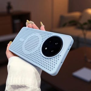 Könnte beinhalten: Eine hellblaue Smartphone-Hülle mit einem perforierten Gittermuster auf der Rückseite. Die Hülle verfügt über eine große, kreisförmige Aussparung auf der oberen rechten Seite für ein Kameramodul mit drei Linsen sowie einen magnetischen Ring.