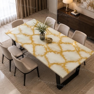 Puede incluir: Una mesa de comedor rectangular con tablero de piedra con patrón blanco y dorado y patas de metal negro, acompañada de seis sillas beige tapizadas. Un jarrón de cristal con follaje verde y un pequeño cuenco dorado están sobre la mesa.