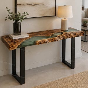 Può includere: Un tavolo console caratterizzato da un piano in legno naturale con bordi irregolari e un inserto centrale in resina verde traslucida. Il tavolo è sostenuto da due gambe in metallo nero a forma di U e presenta venature del legno a vista.