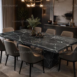 Puede incluir: Una mesa de comedor rectangular con una superficie de mármol negro pulido con vetas blancas, apoyada sobre una base central. La mesa está rodeada por seis sillas tapizadas en un color topo neutro con patas de madera oscura.