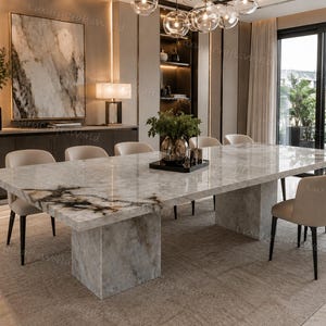 May include: A rectangular dining table with a polished white and grey marble top featuring dark veining, supported by two thick, matching marble pedestal bases. The table is surrounded by six beige upholstered chairs with dark metal legs.