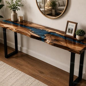 May include: A long console table featuring a natural live-edge wood slab surface with a central translucent blue resin river inlay. The table is supported by two sturdy black metal U-shaped legs, showcasing a polished wood grain finish.