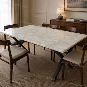 May include: A rectangular dining table with a polished beige marble top and a black metal X-shaped base, accompanied by four wooden chairs featuring dark brown frames and light beige upholstered seats, arranged in a dining room setting.