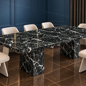 May include: A rectangular dining table featuring a polished black marble top with prominent white veining, supported by two matching black marble pedestal bases, surrounded by six cream-colored upholstered chairs with angled backrests.