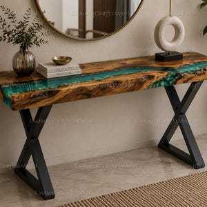 Può includere: Un tavolo console rettangolare con un piano in legno a bordo naturale e un inserto centrale in resina turchese traslucida. Il tavolo è sostenuto da due gambe in metallo nero a forma di X. La venatura del legno è visibile e la resina contiene piccole pietre.