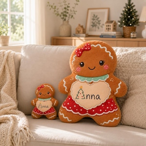 May include: Two brown gingerbread person plush toys with embroidered details. Each features a red bow, a light green collar, and a cream-colored heart on the chest with the name Anna and a green Christmas tree graphic. Both wear a red skirt with white dots.