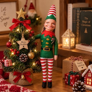 May include: A custom elf doll with a person's face, wearing a green tunic with gold buttons, a black belt, and red and white striped leggings. The elf stands next to a small, lit Christmas tree decorated with red ornaments, a wooden star, and a gold bell.
