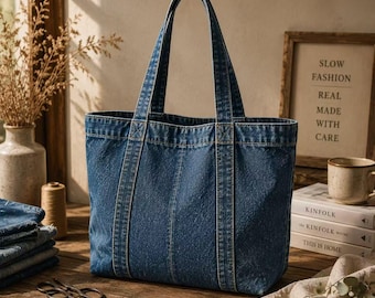 May include: A medium blue denim tote bag with two vertical stitched panels and two long shoulder straps. The bag features a rectangular base and a structured open top design, crafted from durable cotton denim fabric with visible seams.