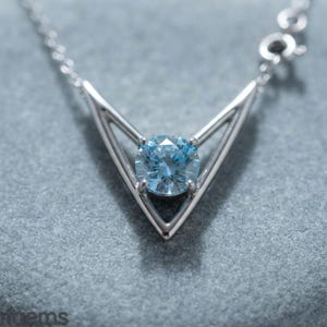 May include: A silver-toned necklace featuring a V-shaped pendant with a central round-cut light blue gemstone. The pendant is suspended from a delicate silver-toned chain, showcasing a clean, geometric design with a polished metallic finish.