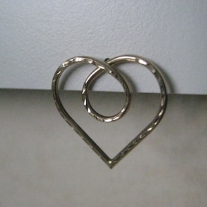 May include: A silver heart-shaped wire sculpture with a smaller circle inside.