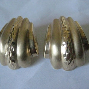 May include: A pair of gold-tone earrings with a textured, ridged design. The earrings are shaped like a shell and have a diamond-shaped pattern.