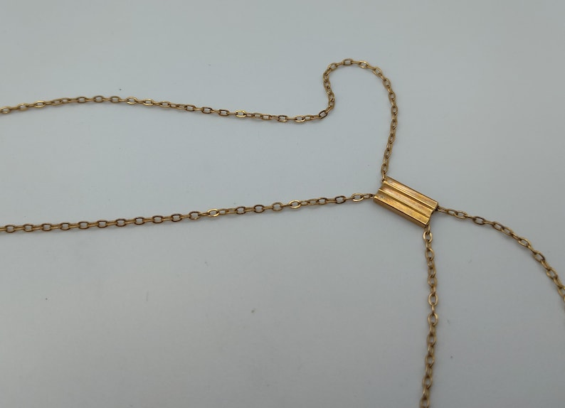 Puede incluir: Collar dorado con un dise&ntilde;o de cadena delicado. El collar presenta un colgante rectangular con tres l&iacute;neas horizontales. La cadena se extiende en forma de Y, creando un aspecto &uacute;nico y elegante.