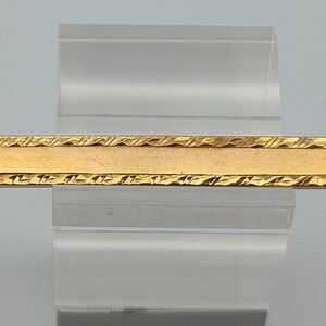May include: A gold tie bar with a textured border.