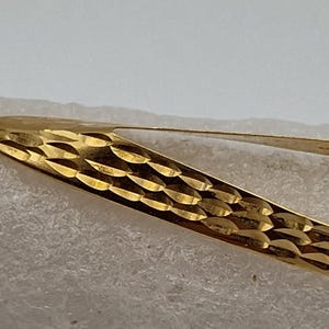 May include: A gold pendant featuring a clear round stone. The pendant is shaped like a teardrop and has a textured surface.