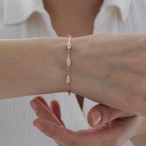 Puede incluir: Una delicada pulsera de oro que presenta una serie de eslabones en forma de marquesa. Cada eslabón está incrustado con pequeñas piedras blancas, alternando con diminutas piedras circulares de color verde vibrante entre las formas.