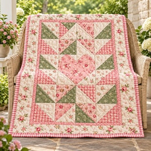 Könnte beinhalten: Eine gesteppte Tagesdecke mit einem zentralen Herzmotiv aus rosafarbenem Blumenstoff. Das Design umfasst dreieckige Blöcke in Salbeigrün und rosafarbenem Vichy-Karo, umrahmt von einer Bordüre aus rosa Rosen auf cremefarbenem Grund.