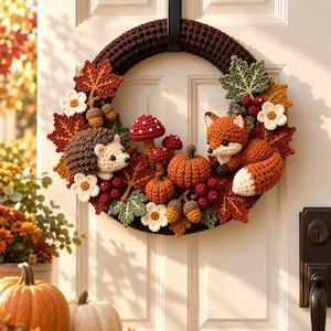 May include: A circular dark brown crochet wreath decorated with handmade yarn figures including a hedgehog, a fox, pumpkins, mushrooms, acorns, red berries, and various autumn-colored leaves in shades of orange, yellow, and green with white flowers.