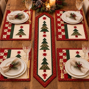 May include: A quilted table runner and four matching placemats featuring a Christmas tree and star pattern in red, green, and cream. The set includes white plates, gold-toned cutlery, and napkins adorned with small pine sprigs and red berries.