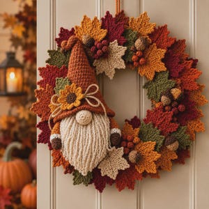 Op de afbeelding: Een gehaakte krans met een kabouter met een hoge oranje muts, een crèmekleurige baard en een zonnebloemaccent. De krans is versierd met diverse gehaakte herfstbladeren in tinten rood, oranje, geel en groen, samen met kleine bruine eikeltjes.
