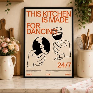 May include: A framed rectangular wall art print with a cream background and black frame. The text reads THIS KITCHEN IS MADE FOR DANCING 24/7. It features black line art of hands holding a vinyl record and a wine glass, with the words DANCE COOK REPEAT.