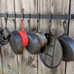 Pot rack is mounted on a barnwood wall and shown displaying 8 pieces of vintage Griswold cast iron.