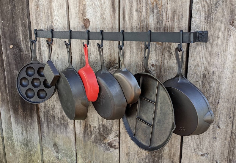Pot rack is mounted on a barnwood wall and shown displaying 8 pieces of vintage Griswold cast iron.