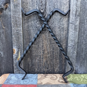 May include: Two black metal fireplace tools with twisted handles. The tools are crossed and leaning against a wooden wall.