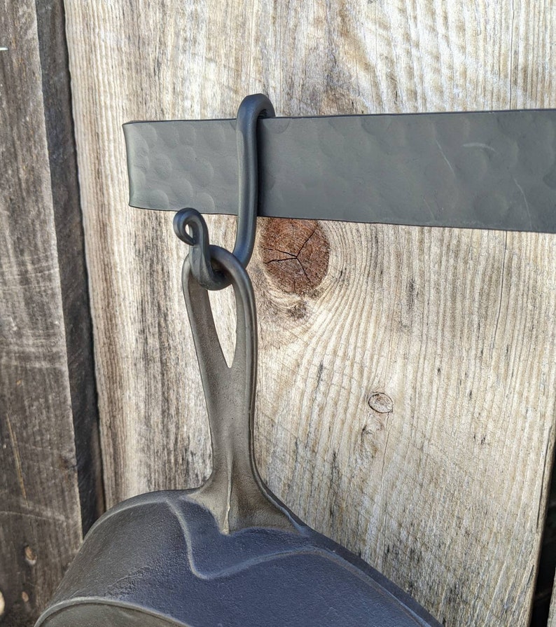 Close up of the scroll style hook with the handle of a cast iron pan it is supporting.