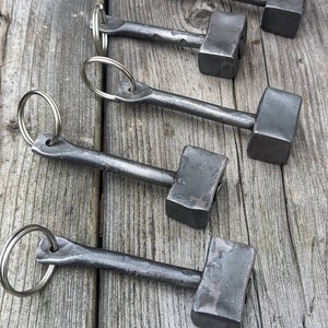 Puede incluir: Cinco llaveros de martillo de metal plateado con anillos de llave plateados. Los martillos son de diferentes tamaños y tienen un acabado ligeramente texturizado.