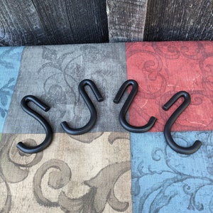 May include: Four black metal hooks with a simple S-shape design. The hooks are arranged in a row on a patterned fabric surface.