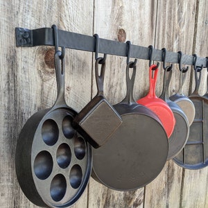 Side view of pot rack on barnwood wall holding a variety of cast iron pans.