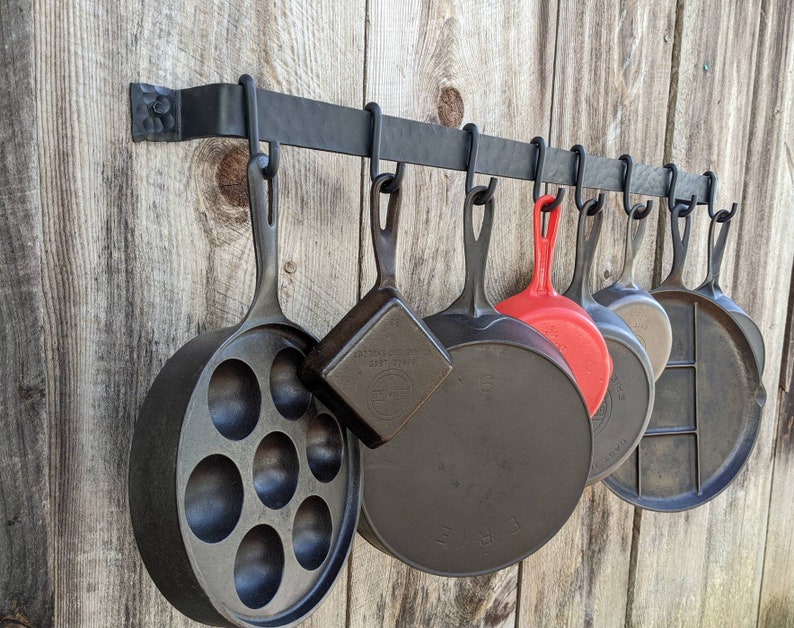 Side view of pot rack on barnwood wall holding a variety of cast iron pans.