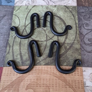 Può includere: Quattro ganci in metallo nero con un design a forma di S unico. I ganci sono disposti in due coppie, con i ganci di ogni coppia rivolti in direzioni opposte.