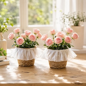 Puede incluir: Dos cestas de mimbre trenzado que contienen rosas de color rosa claro, cada una adornada con un borde de volantes de tul blanco transparente en la parte superior. Las cestas están llenas de follaje verde y varias rosas en flor.