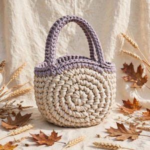 May include: A round, hand-crocheted basket bag featuring a thick, cream-colored cord body with a circular base pattern and a contrasting lavender-colored top rim and handle. The bag is constructed from chunky, braided textile yarn.