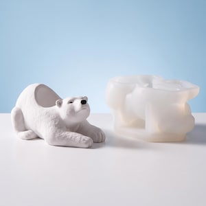 May include: A white polar bear figurine with a hollow back for storage and a matching translucent silicone mold. The bear has a textured surface, a black nose, and is in a reclining position. The mold is shaped to create the bear figure.