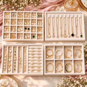 May include: Four beige velvet jewelry organizer trays containing a collection of gold-tone jewelry, including various stud earrings, necklaces with pendants, delicate bracelets, and rings featuring pearls, crystals, and green stones.