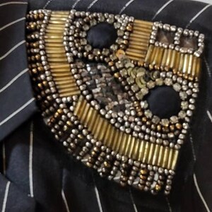 Pode incluir: Um blazer listrado preto e branco com um enfeite de contas douradas e prateadas no ombro.