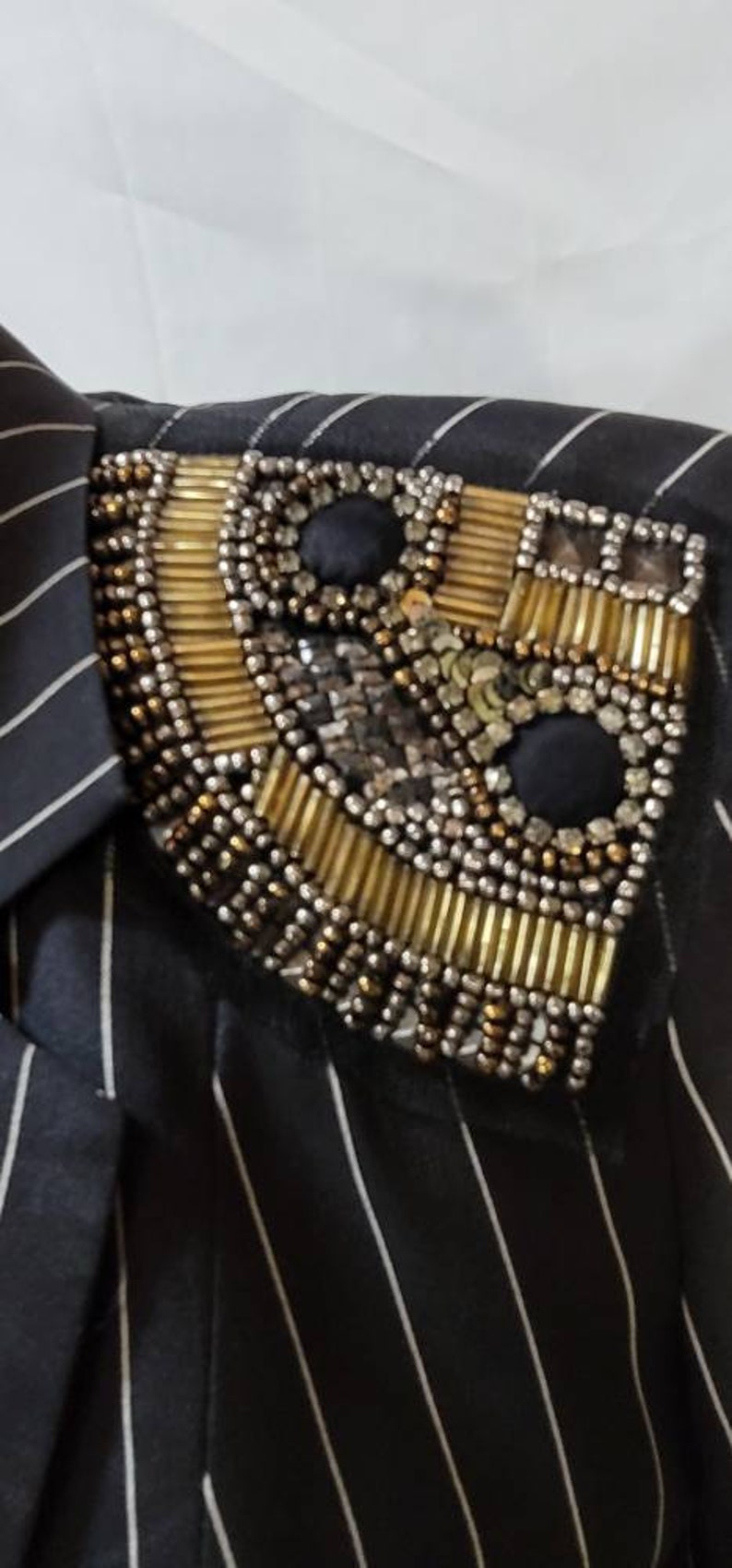 Pode incluir: Um blazer listrado preto e branco com um enfeite de contas douradas e prateadas no ombro.