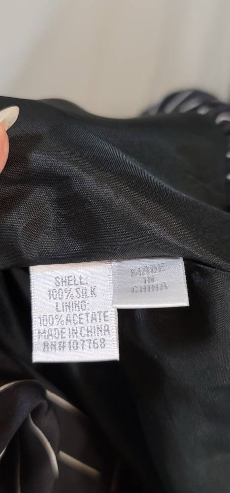 Pode incluir: Uma etiqueta branca com texto preto que diz "SHELL: 100% SILK LINING: 100% ACETATE MADE IN CHINA RN#107768" e uma etiqueta branca menor com texto preto que diz "MADE IN CHINA".